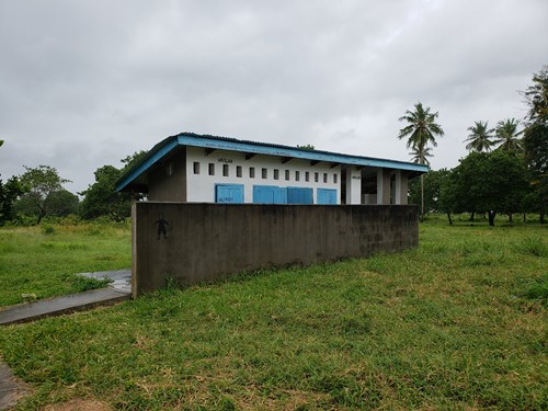 Small building containing the latrines in an open patch of grass with a sidewalk leading up to the building