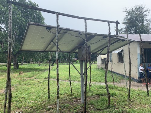 A solar panel rigged up with thin, wooden posts outside of the a school 
