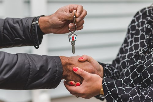 Two people shaking hands & one of them handing over keys to the other. 