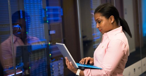 Woman standing with computer in hand, focused on screen. 